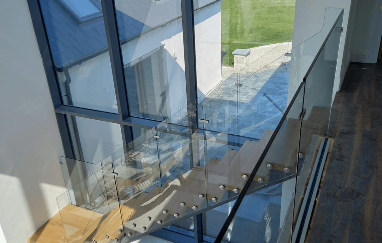 Landing And Stair Glass Panels Bolted On Modern Staircase With Glass Panels And Wooden Steps In A Sunlit Interior.