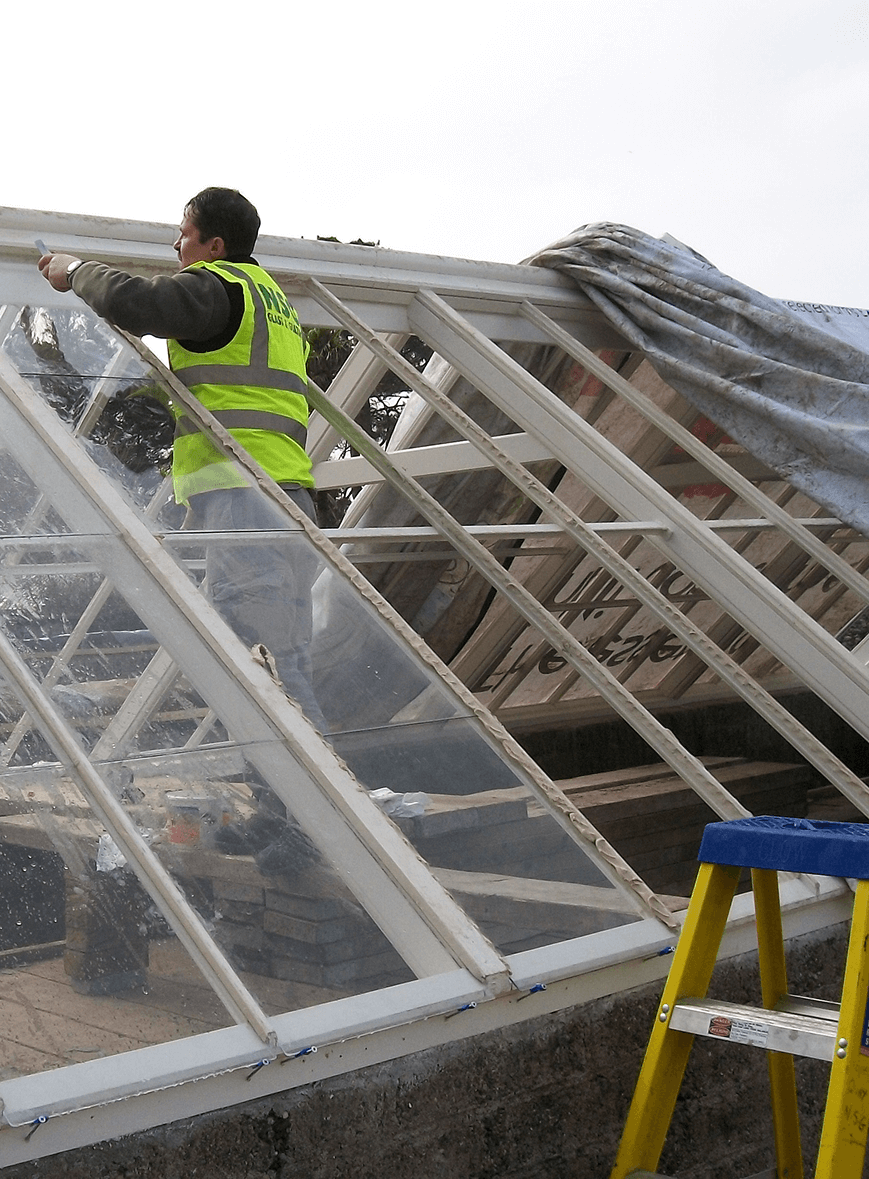 Greenhouse Glass Worker In High-Visibility Vest Installing Glass Panels On Greenhouse Roof