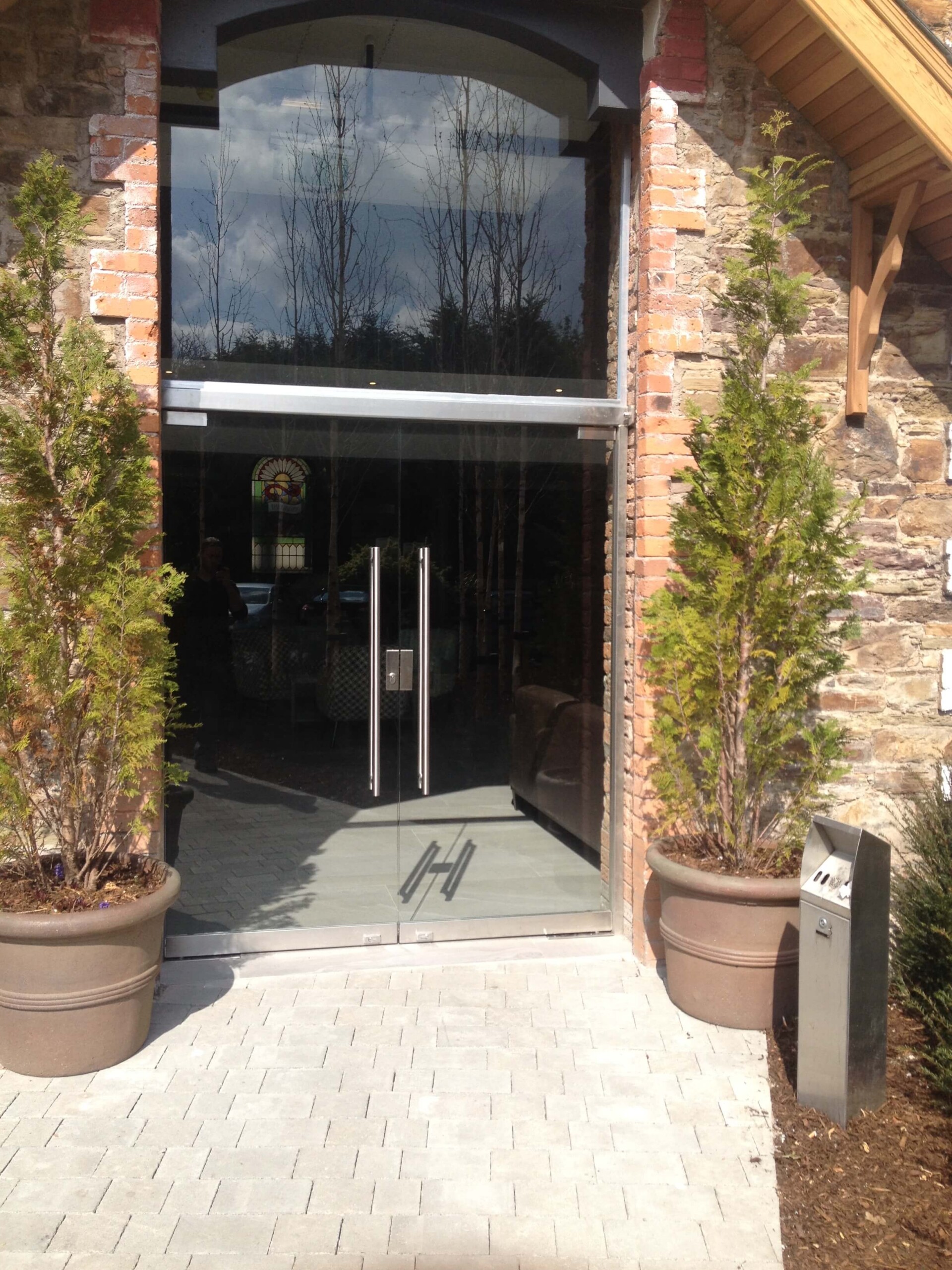 Swing Doors In Toughened Glass Glass Swing Doors With Metal Handles At Brick-Framed Building Entrance