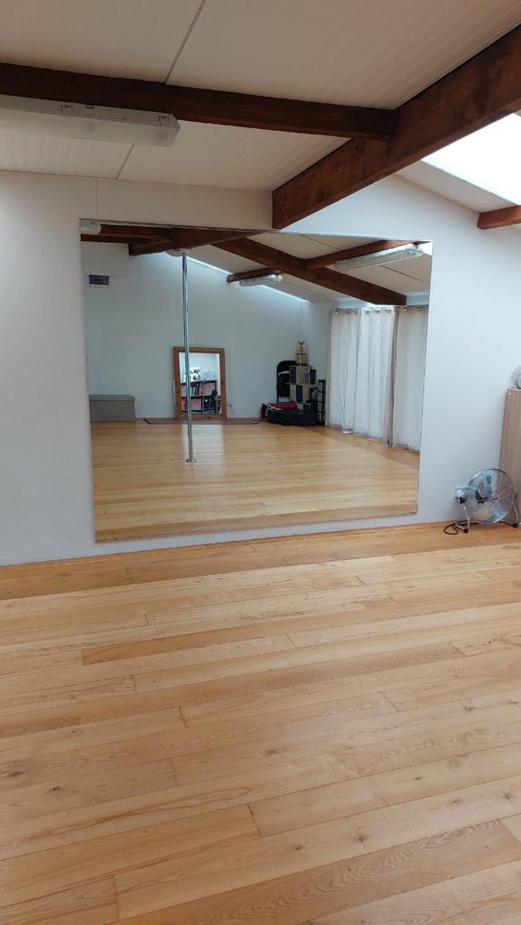 Spacious Room With Wooden Flooring, Exposed Ceiling Beams, And Large Mirror